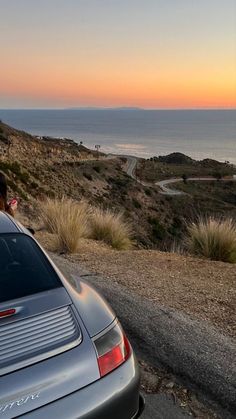 a car parked on the side of a road next to the ocean at sunset or sunrise