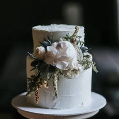 a white wedding cake with flowers and greenery on the top is sitting on a plate