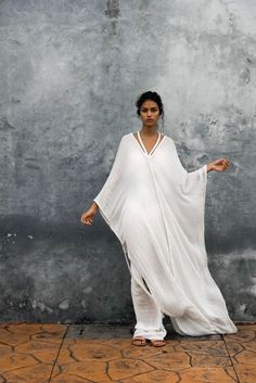 Airy and fluid in design, a classic Kasia Kulenty silhouette to celebrate subtlety. Modest and modern, this winged kaftan is trimmed generously with our signature handwoven braids. Uniquely designed with a pendant neckline detail… slip it off the shoulders to create a luxurious cape-like gown. Eternally chic!100% Cotton. Model is wearing hand-dyed hue Nube.Each garment is handmade to order and designed unisize to fit many different body types, as well as individually hand-dyed in a non-toxic and Kaftan Gown, Fabric Draping, Goddess Gown, Kaftan Designs, Cotton Gauze Fabric, Mode Boho, Goddess Braids, Kaftan Dress, Draped Fabric