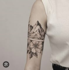 a woman's arm with flowers on it and mountains in the distance behind her