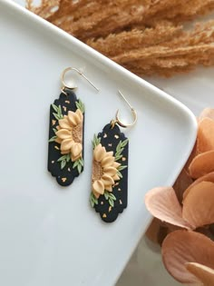 pair of earrings with sunflowers and leaves on them sitting next to dried flowers