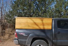 a pickup truck with a wood panel in the bed parked on a dirt road next to some trees