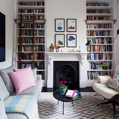 a living room filled with furniture and bookshelves next to a fire place under a window