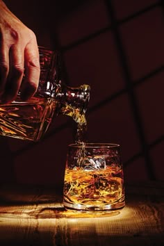 someone pouring whiskey into a glass on top of a wooden table