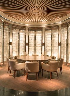 a round dining room table surrounded by beige chairs and wooden ceilinging with glass panels