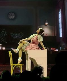 a woman sitting on top of a yellow chair in front of a stage with an audience