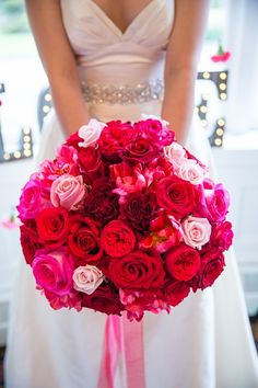 a bride holding a large bouquet of red and pink flowers in her wedding day dress