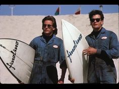 two men in overalls are holding surfboards