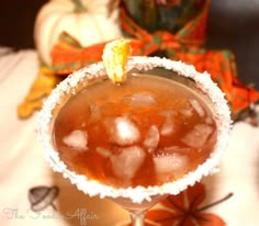 a glass filled with ice sitting on top of a table next to an orange pumpkin