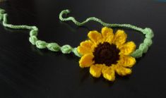 a crocheted sunflower is shown on a black surface with green string and brown center