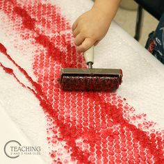 a child using a paint roller to create a red and white pattern on the table