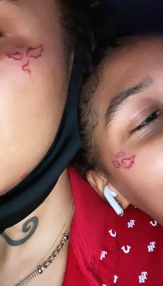 two people with tattoos on their faces are laying next to each other and one is wearing a red shirt