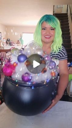 a woman with green hair is holding a large black bowl filled with balls and ornaments