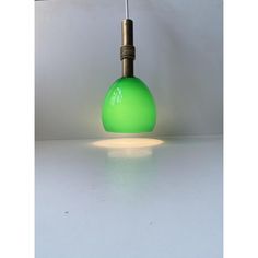 a green light hanging from a ceiling fixture on a white table with a black cord