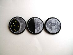 three embroidered patches depicting the phases of an earth's moon and sun, on a white surface