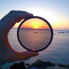 a person holding up a magnifying glass to look at the sunset over water