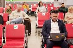 a man sitting on a red chair with his laptop in front of him while others sit behind him