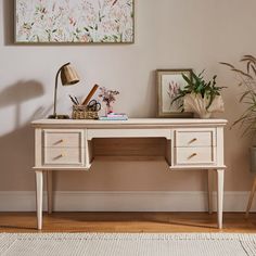 a white desk with two drawers and a lamp on it in a living room next to a plant