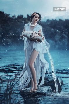 a woman is standing in the water wearing a white dress and holding an arm around her body