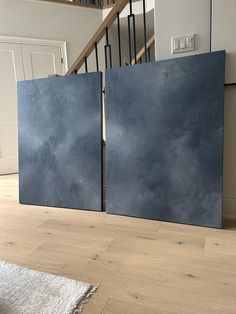 two large black doors sitting on top of a wooden floor next to a stair case