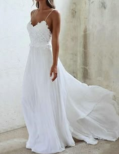 a woman wearing a white dress standing in front of a wall and looking at the camera