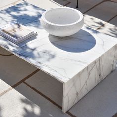 a marble table with a white bowl on top and some books next to it in the sun