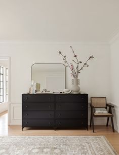 a room with a large mirror, black dresser and white rug on the wooden floor