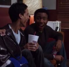 two young men sitting next to each other on a couch and one holding a drink