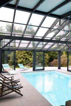 an indoor swimming pool surrounded by glass walls and doors, with lounge chairs around it