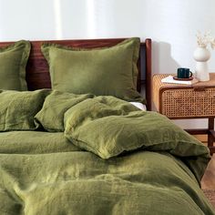 a bed with green sheets and pillows in a room next to a night stand, wicker side table