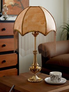 a table lamp sitting on top of a wooden table next to a cup and saucer