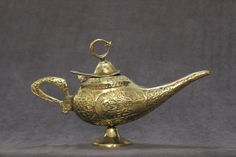 a gold teapot with a handle and lid on a stand, in the shape of a fish