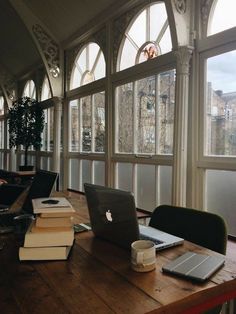 there are many laptops and books on the table in front of large windows that look out onto the city