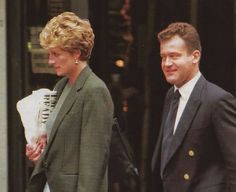 the man and woman are walking together in front of an office building, one is wearing a suit