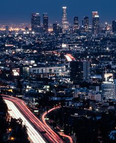 an aerial view of the city at night with light trails in the foreground and skyscrapers lit up