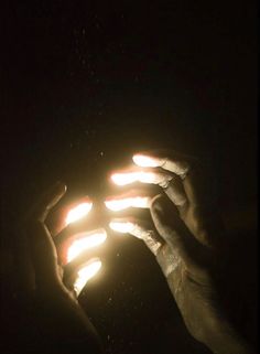 two hands holding lit candles in the dark