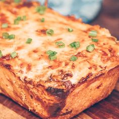 a cheesy casserole with green onions on top is sitting on a cutting board