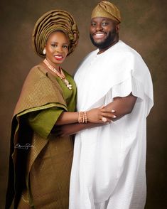 a man and woman posing for a photo in front of a brown background wearing traditional african clothing