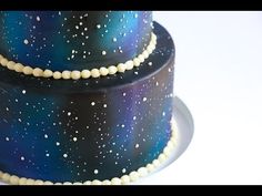 a three tiered blue and black cake with white stars on the top, sitting on a plate