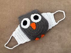 a crocheted owl hat with two eyes and an orange nose is laying on a brown surface