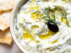 an image of a bowl of dip with olives and pita chips on the side