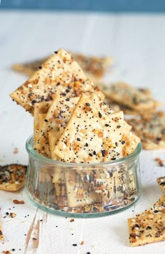 some crackers are in a glass bowl on a white tablecloth and scattered with black seeds