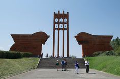 people are standing in front of two large sculptures on the side of a road with stairs leading up to them