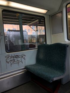 an empty seat on a subway train with graffiti written on the wall and windows behind it