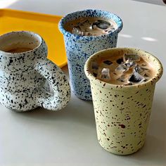 three ceramic mugs sitting on top of a table next to each other with liquid in them