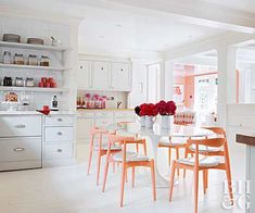 a kitchen filled with lots of white furniture and pink flowers on top of the table