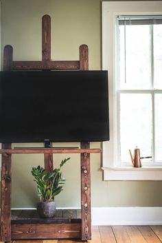 a tv sitting on top of a wooden stand in front of a window with a potted plant