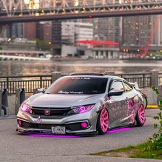 a gray car with pink rims parked in front of a bridge and some buildings