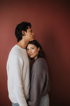 two people standing next to each other in front of a red wall and one person is hugging