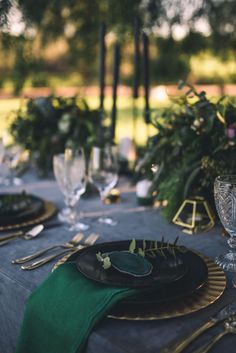 the table is set with black plates and green napkins, silverware, and greenery